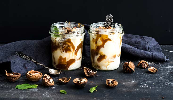 Two jars of pudding with a spoon and walnuts.