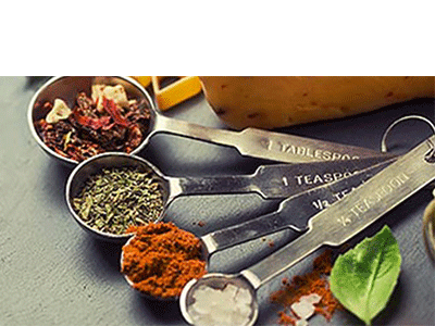 A row of measuring spoons filled with a variety of Greek herbs and spices